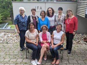 6 Frauen stehend in Kamera lächelnd, davor 3 Frauen auf einer Bank sitzend